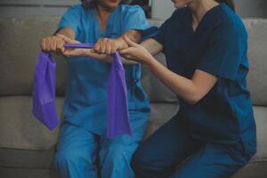 personnel entraîneur assistant Sénior femme avec la résistance groupe. réhabilitation physiothérapie ouvrier portion vieux patient à allaitement maison. vieux femme avec étendue bande étant coaché par physiothérapeute. photo