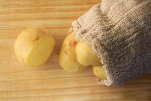 pomme de terre qui sort du sac sur une table en bois, pomme de terre coupée photo