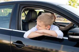 le mignonne garçon grimpé en dehors de le voiture fenêtre et regards loin. aller avec papa dans le voiture photo