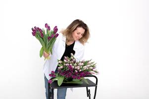 une charmant fille penché plus de une table avec différent variétés de tulipes. bouquet de violet tulipes photo