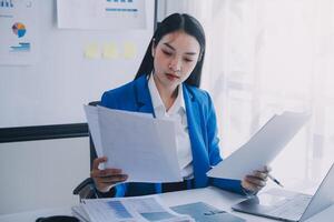 femme d'affaires joyeuse travaillant sur un ordinateur portable au bureau, belle femme d'affaires heureuse asiatique en costume formel travaille sur le lieu de travail. jolie employée de bureau souriante. photo