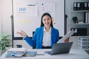 femme d'affaires joyeuse travaillant sur un ordinateur portable au bureau, belle femme d'affaires heureuse asiatique en costume formel travaille sur le lieu de travail. jolie employée de bureau souriante. photo