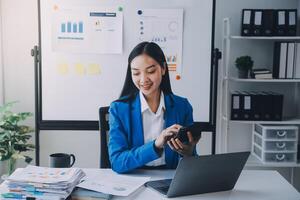 femme d'affaires joyeuse travaillant sur un ordinateur portable au bureau, belle femme d'affaires heureuse asiatique en costume formel travaille sur le lieu de travail. jolie employée de bureau souriante. photo