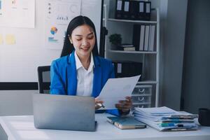 femme d'affaires joyeuse travaillant sur un ordinateur portable au bureau, belle femme d'affaires heureuse asiatique en costume formel travaille sur le lieu de travail. jolie employée de bureau souriante. photo