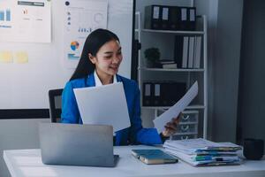 femme d'affaires joyeuse travaillant sur un ordinateur portable au bureau, belle femme d'affaires heureuse asiatique en costume formel travaille sur le lieu de travail. jolie employée de bureau souriante. photo