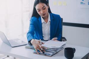 femme d'affaires joyeuse travaillant sur un ordinateur portable au bureau, belle femme d'affaires heureuse asiatique en costume formel travaille sur le lieu de travail. jolie employée de bureau souriante. photo