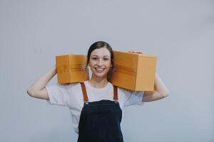 souriant asiatique femme dans décontractée vêtements en portant une papier carton boîte maquette tandis que permanent contre un isolé blanc Contexte. livraison affaires concept photo