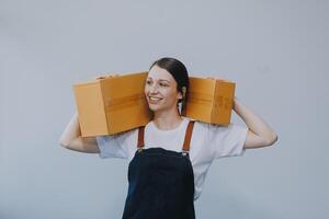 souriant asiatique femme dans décontractée vêtements en portant une papier carton boîte maquette tandis que permanent contre un isolé blanc Contexte. livraison affaires concept photo