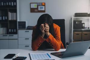 portrait de fatigué Jeune affaires asiatique femme travail avec les documents impôt portable ordinateur dans bureau. triste, malheureux, inquiet, dépression, ou employé la vie stress concept photo