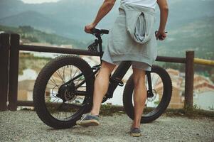 tondu portrait de une Jeune Masculin cycliste, permanent près le sien électrique vélo, ayant une Pause après Cyclisme dans montagnes. personnes. actif en bonne santé mode de vie. vélo électrique comme durable, éco amical transport photo