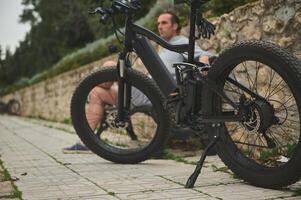 sélectif concentrer sur un innové moderne noir électrique vélo, garé près une banc avec une séance cycliste photo