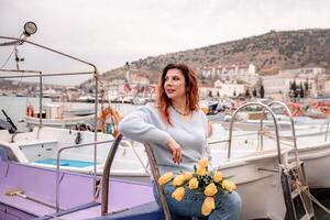 femme détient Jaune tulipes dans port avec bateaux amarré dans le arrière-plan., couvert jour, Jaune chandail, montagnes photo