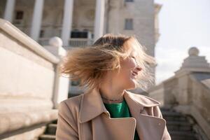 une femme avec longue cheveux est permanent sur une ensemble de escaliers. elle est portant une vert chemise et une bronzer manteau. photo