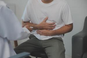 homme Souffrance avec sévère estomac douleur séance à maison. main de mature gars en portant abdomen Souffrance de mal, la diarrhée ou indigestif problème. caucasien gars pressage sur ventre sur douloureux sensation photo