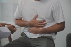 homme Souffrance avec sévère estomac douleur séance à maison. main de mature gars en portant abdomen Souffrance de mal, la diarrhée ou indigestif problème. caucasien gars pressage sur ventre sur douloureux sensation photo