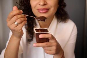 fermer de une flou Jeune souriant femme en mangeant délicieux Chocolat végétalien yaourt pour petit déjeuner. en bonne santé en mangeant et régime concept. nourriture et boisson consumérisme. photo