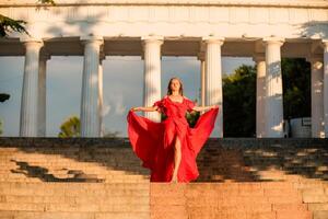 une femme dans une longue rouge robe contre le toile de fond de lever du soleil, brillant d'or lumière de le du soleil des rayons. le concept de la féminité, harmonie. photo