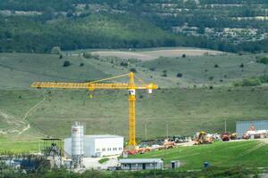 une grand grue est sur une construction site dans une rural zone. le grue est Jaune et est entouré par une lot de autre construction équipement. le scène est paisible et calme. photo