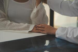 médecin donnant espoir. proche en haut coup de Jeune femelle médecin penché vers l'avant à souriant personnes âgées Dame patient en portant sa main dans palmiers. femme le concierge dans blanc manteau justificatif encourageant vieux la personne photo