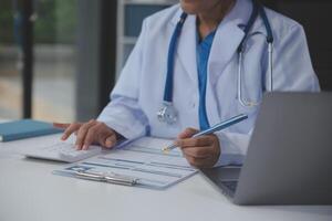 une professionnel et concentré asiatique femelle médecin dans gommages est travail et en train de lire médical recherche sur sa portable dans sa Bureau à une hôpital. photo