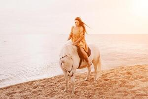 une femme dans une robe des stands suivant à une blanc cheval sur une plage, avec le bleu ciel et mer dans le Contexte. photo
