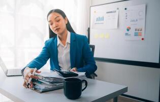 femme d'affaires joyeuse travaillant sur un ordinateur portable au bureau, belle femme d'affaires heureuse asiatique en costume formel travaille sur le lieu de travail. jolie employée de bureau souriante. photo