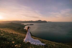 une femme des stands sur une colline surplombant le océan dans une longue blanc robe photo