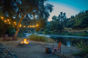 paisible au bord de la rivière site de camp illuminé par le vacillant lumière de feu de camp photo