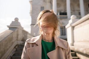 une femme avec longue cheveux est permanent sur une ensemble de escaliers. elle est portant une vert chemise et une bronzer manteau. photo