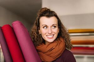 joyeux expression capturé sur une femme avec frisé cheveux, portant une chaud foulard, avec coloré en tissu Rouleaux dans le Contexte photo