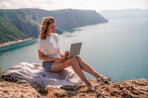 free-lance femmes mer travail sur le ordinateur. bien à la recherche milieu vieilli femme dactylographie sur une portable clavier en plein air avec une magnifique mer voir. le concept de éloigné travail. photo