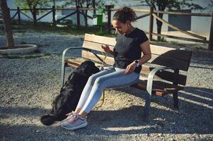 Jeune athlétique femme relaxant séance sur le banc, en marchant sa chien tandis que le jogging dans le Matin dans le la nature. animaux domestiques concept. gens et national animaux. en bonne santé actif mode de vie concept photo