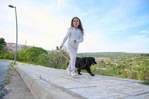 content enfant fille profiter en marchant sa chien en plein air dans le la nature. jolie école âge enfant prise sa pedigree noir cocker épagneul chien pour une marcher sur ensoleillé journée photo