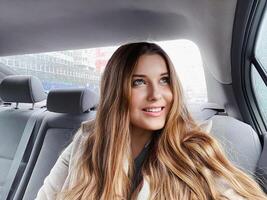 Jeune femme avec longue cheveux, ondulé coiffure dans le voiture ou Taxi taxi comme passager, explorant le ville, transport et Voyage photo