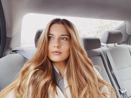 Jeune femme avec longue cheveux, ondulé coiffure dans le voiture ou Taxi taxi comme passager, explorant le ville, transport et Voyage photo