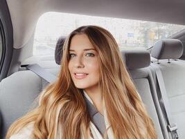 Jeune femme avec longue cheveux, ondulé coiffure dans le voiture ou Taxi taxi comme passager, explorant le ville, transport et Voyage photo