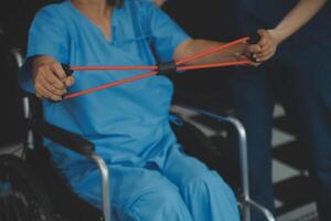 personnel entraîneur assistant Sénior femme avec la résistance groupe. réhabilitation physiothérapie ouvrier portion vieux patient à allaitement maison. vieux femme avec étendue bande étant coaché par physiothérapeute. photo