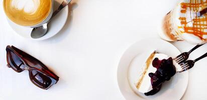 Haut vue de tranche de myrtille cheesecake sur blanc plat ou plaque, marron des lunettes de soleil, chaud cappuccino et glacé caramel macchiato à café avec copie espace. sucré dessert et fait maison aliments. photo