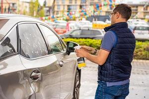 Jeune homme s'applique liquide à nettoyer les fenêtres de le voiture dans en libre service voiture laver. haute qualité photo