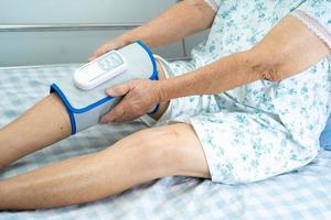 patiente asiatique âgée ou âgée avec un massage des jambes par compression d'air sans fil sur le lit d'un hôpital de soins infirmiers. photo