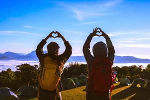 amoureux des femmes et des hommes asiatiques voyagent se détendre pendant les vacances. se lever pour le lever du soleil sur la montagne, joyeuse lune de miel, leva la main pour faire une forme de coeur. photo