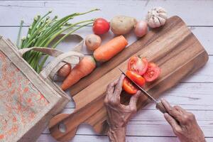 Haut vue de Sénior femme Coupe Frais tomate sur une couper planche à cuisine photo