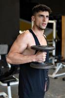 jeune et bel homme athlète faisant des exercices avec des haltères dans la salle de gym photo
