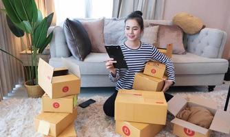 marketing en ligne, jeune propriétaire de petite entreprise en démarrage écrivant l'adresse sur une boîte en carton à partir de l'ordre de la liste. PME entrepreneur de petite entreprise ou femme asiatique indépendante travaillant avec une boîte à la maison photo