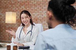 belle femme médecin en chemise blanche qui est une personne asiatique avec stéthoscope examine la santé d'un patient masculin dans une clinique médicale sur fond de mur de briques, souriant conseillant une profession de spécialiste médical. photo