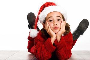 Adorable petite fille portant un bonnet de noel allongé sur un plancher en bois photo