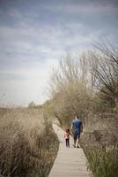 père et petite fille marchant sur un chemin de planches de bois dans une zone humide
