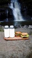 deux hamburgers et deux bouteilles de boissons au bord de la cascade