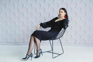 femme portant une robe noire est assise à la chaise en studio blanc photo