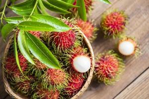 ramboutan frais et mûrs fruits tropicaux sucrés ramboutan pelé avec des feuilles, fruit de ramboutan sur panier et récolte de fond en bois du jardin photo